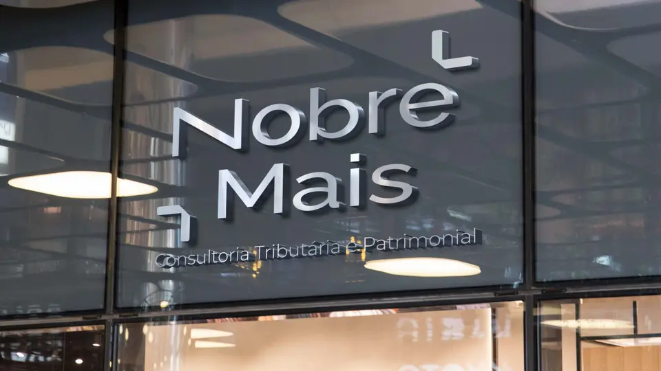 Letreiro da Nobre Mais iluminado na fachada de vidro do escritório, à noite.